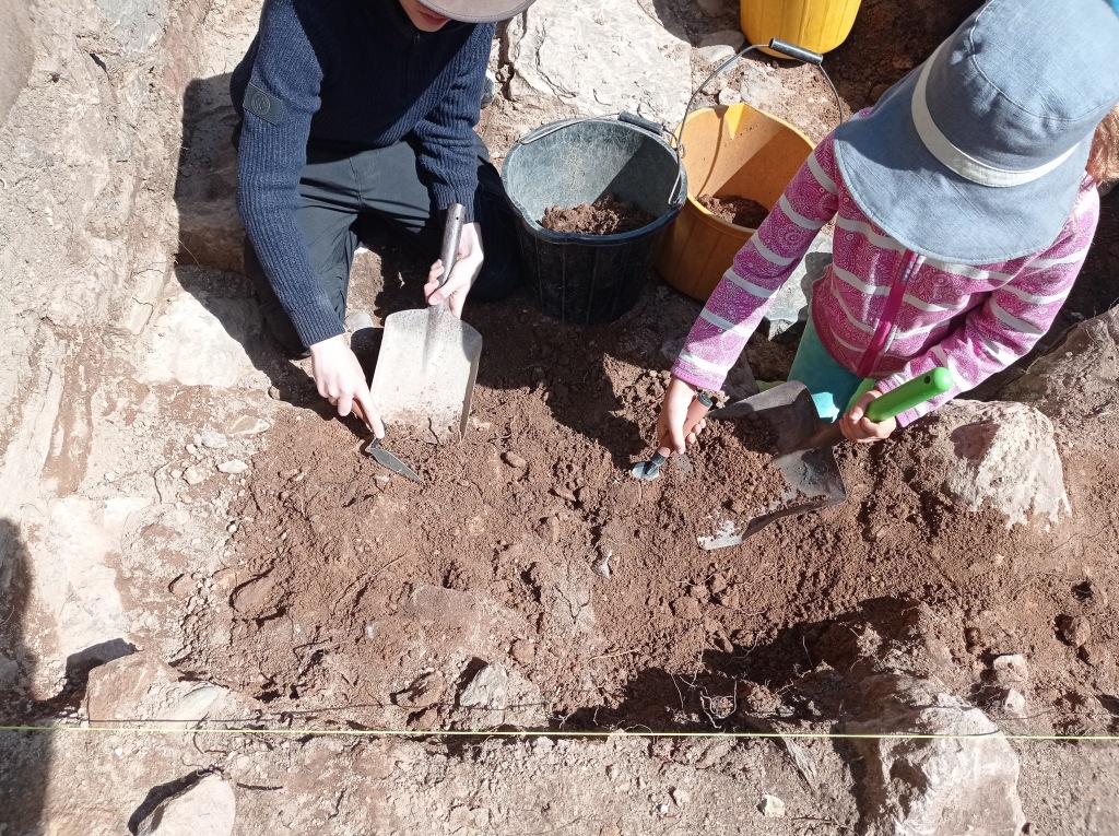A boy and girl slowly level off their section of the trench by removing soil and rocks.